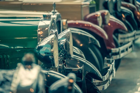 Row of polished classic cars with gleaming chrome headlights and fenders on display at an auto show