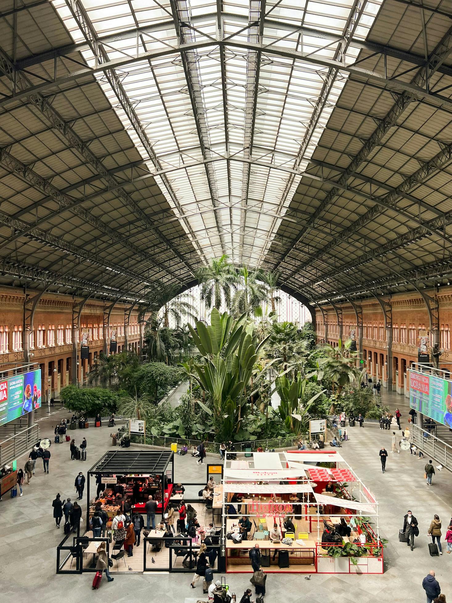 Atocha Train Station in Madrid, featuring its indoor tropical garden, travelers, and seating areas