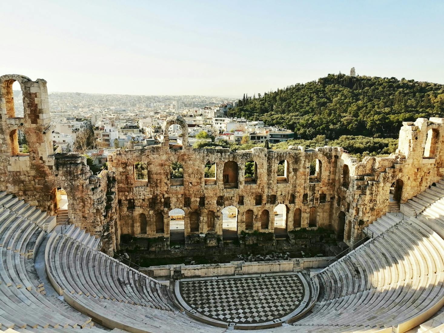 Aerial view of the Roman Theatre in Athens with city building and a forest in the background