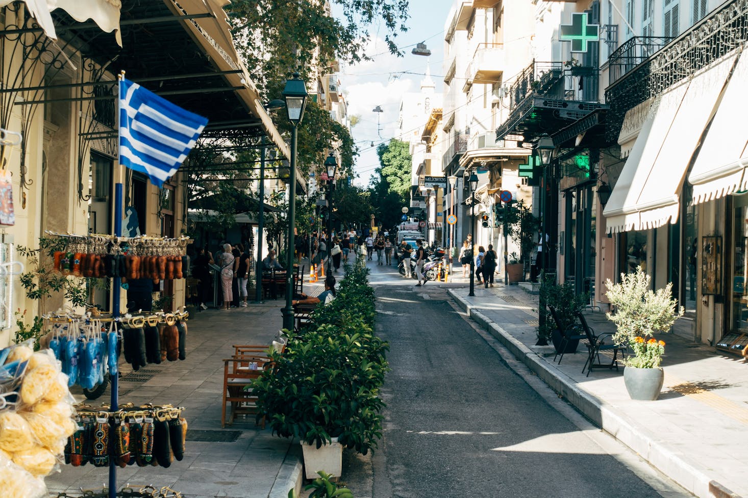 Urban street in Athens, with shops, pedestrians, and sunlit buildings on a clear day