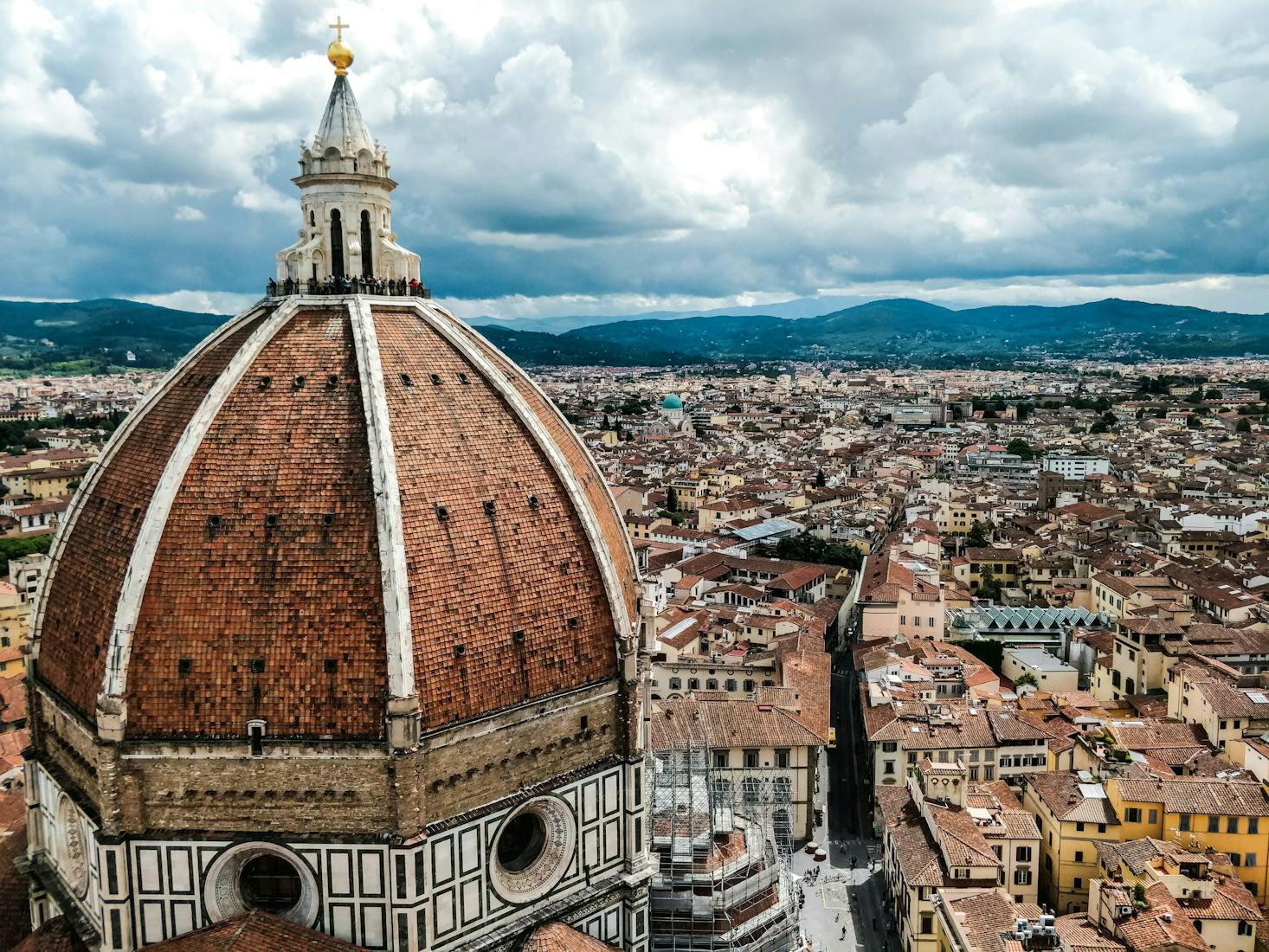 Brown and white Florence Cathedral, cityscape, and mountains under a cloudy sky