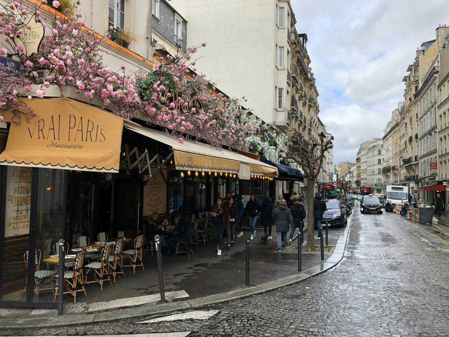 A flowery street in Paris with a café and people walking