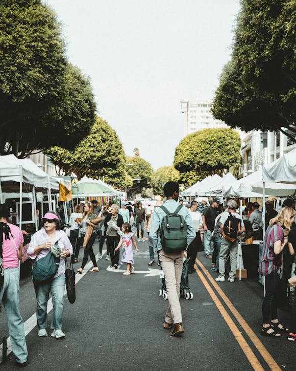 People walking through an open market, with white stalls on the side of the road