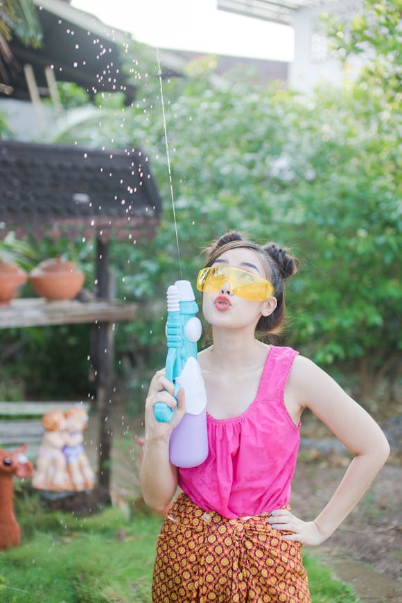 Young woman holding a squirt gun while standing in a yard during Songkran