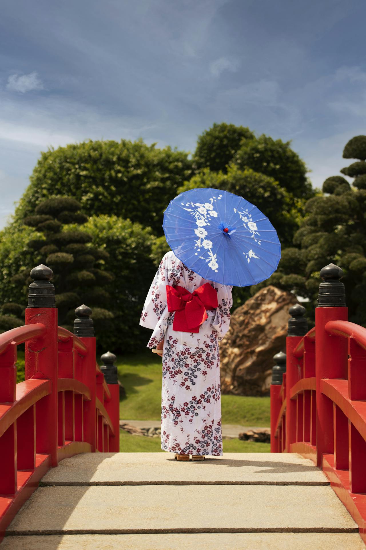 Woman wearing a kimono and carrying a wagasa umbrella while walking over a romantic bridge in Japan