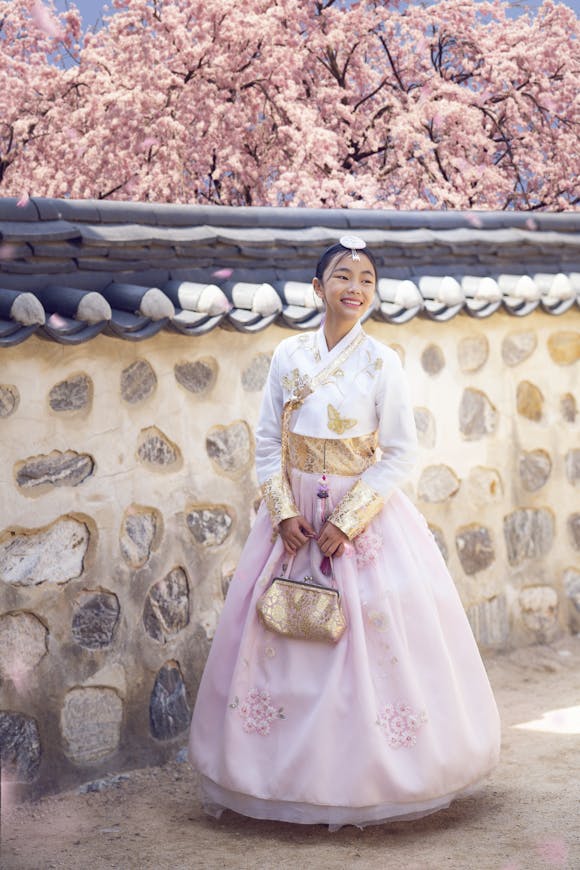 A girl wearing a traditional Korean dress standing under cherry blossoms