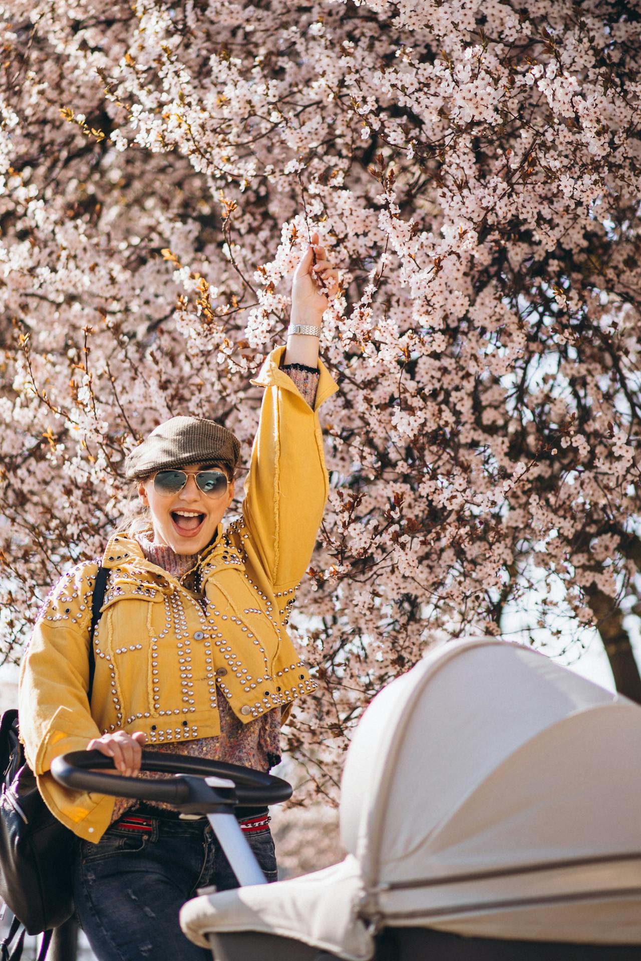 Young mother walking with baby carriage with cherry blossom behind her