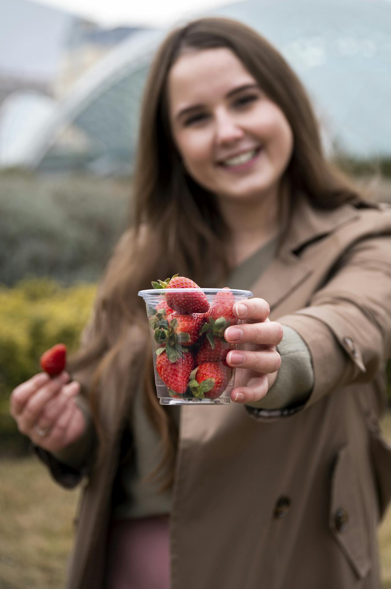 A girl standing outdoors and holding a cup of fresh strawberries