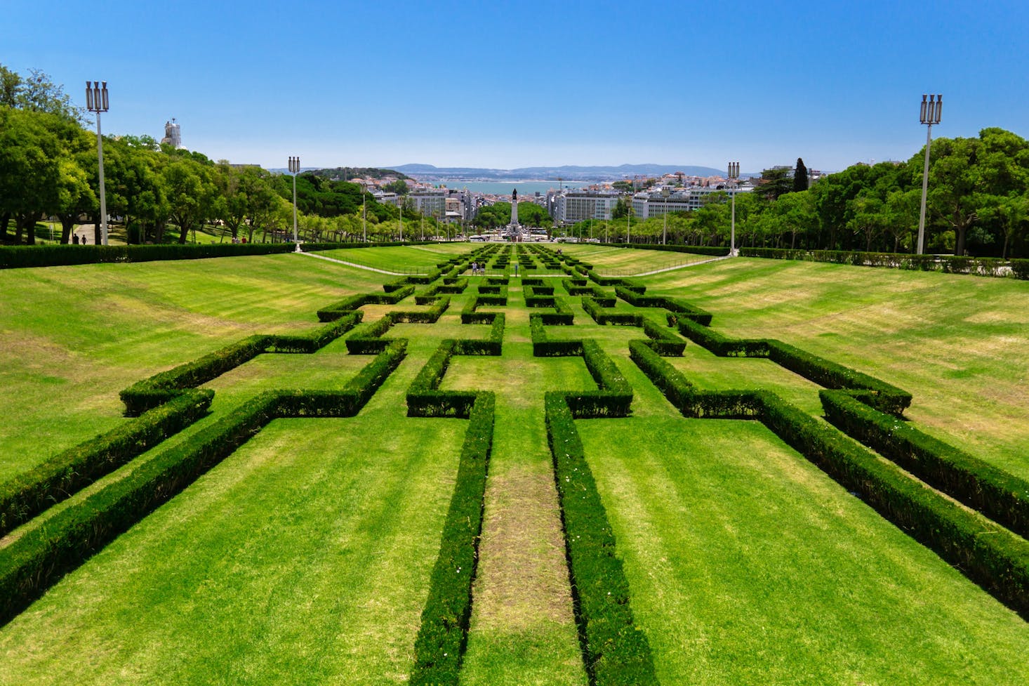 A large park in Lisbon with long maze-style hedges and a monument in the background