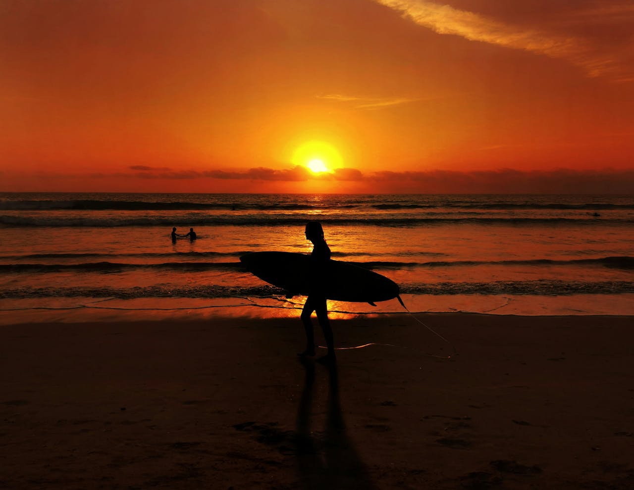 Kuta Beach at sunset with a surfer walking along the sand