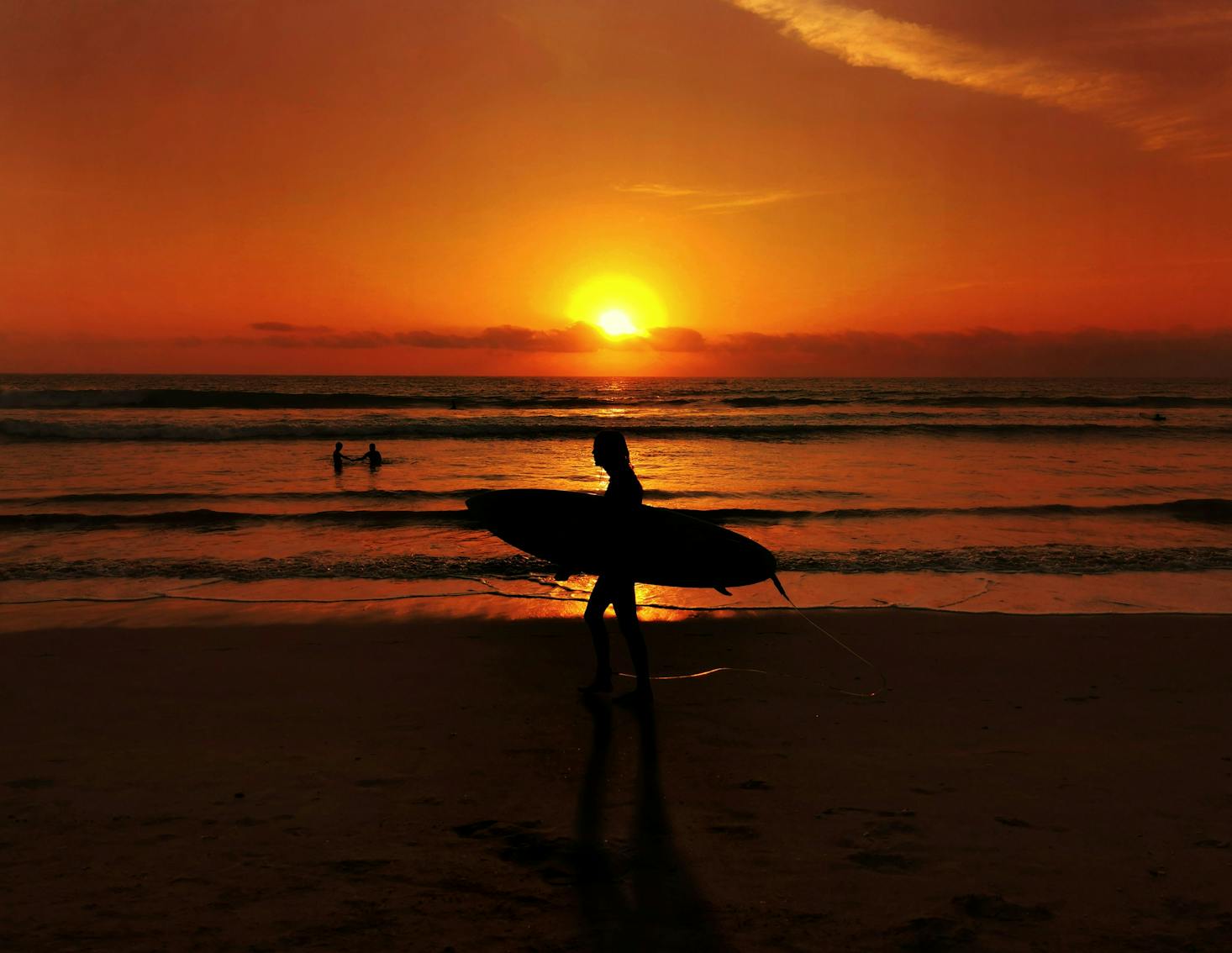 Kuta Beach at sunset with a surfer walking along the sand