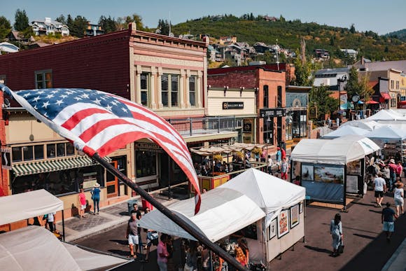 An American flag in front of a busy city street filled with art, vendors and people