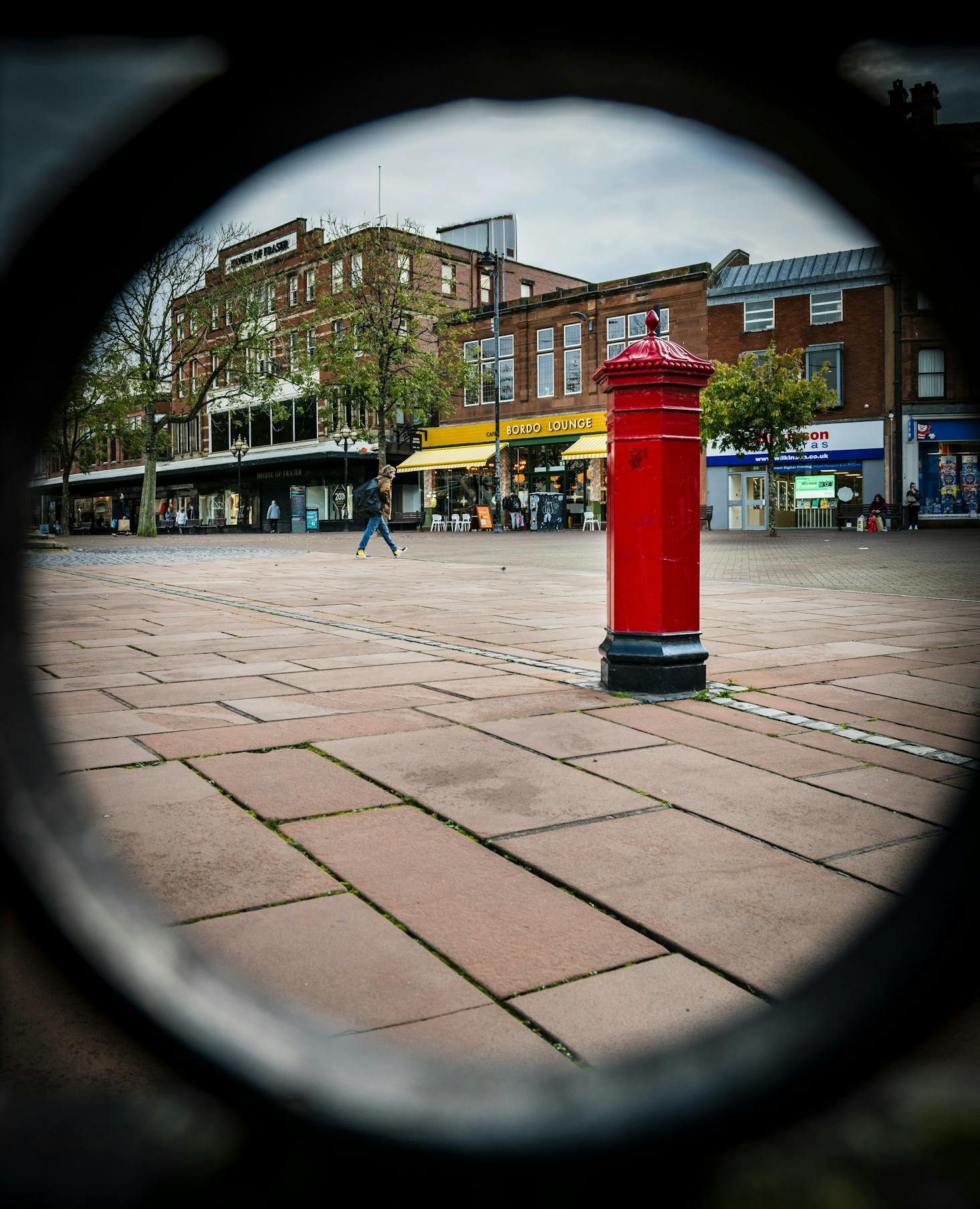 A classic red British postbox stands prominently in a quiet town square of Carlisle.