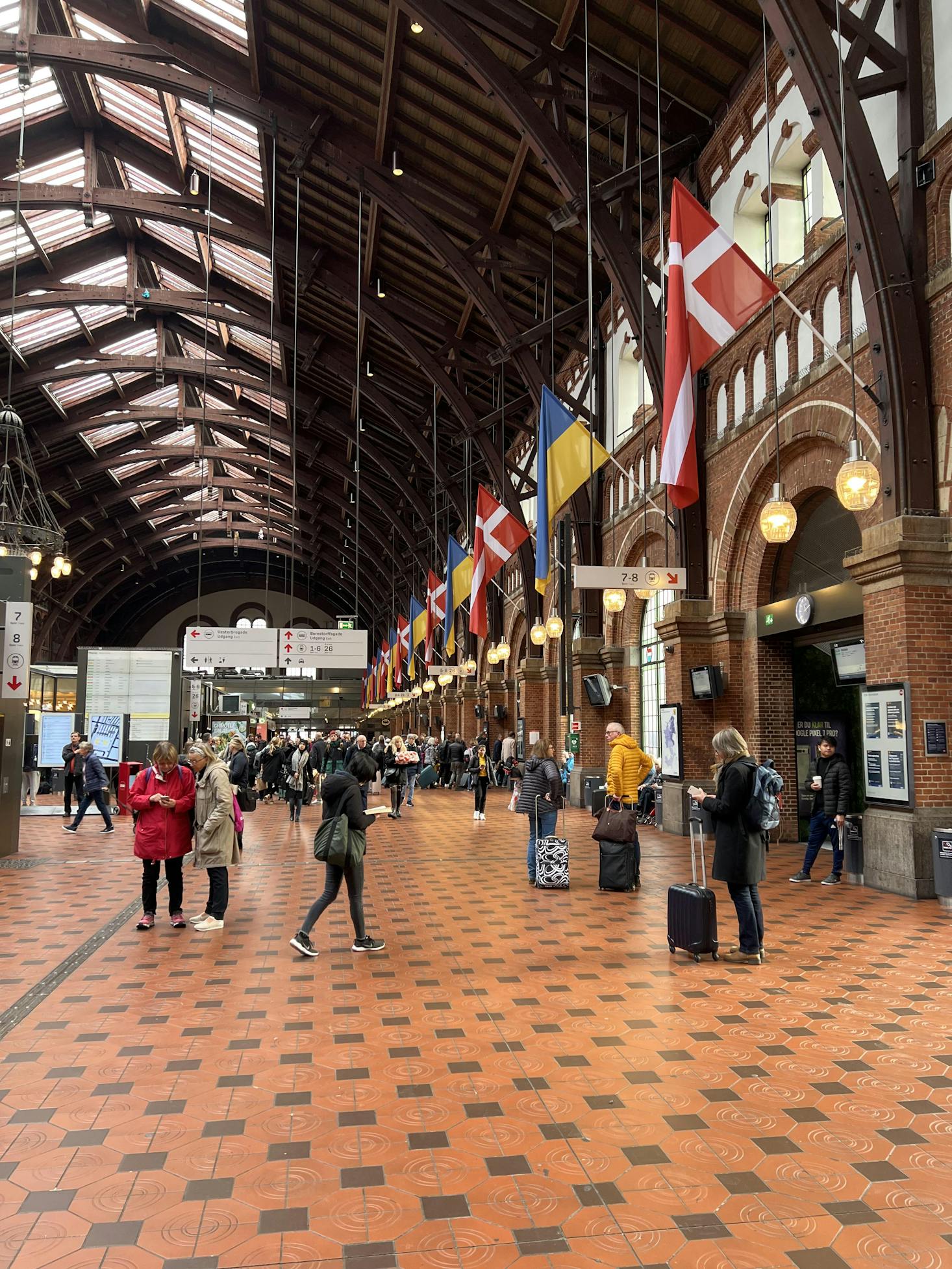 The bustling interior of Copenhagen Central Station, adorned with international flags.