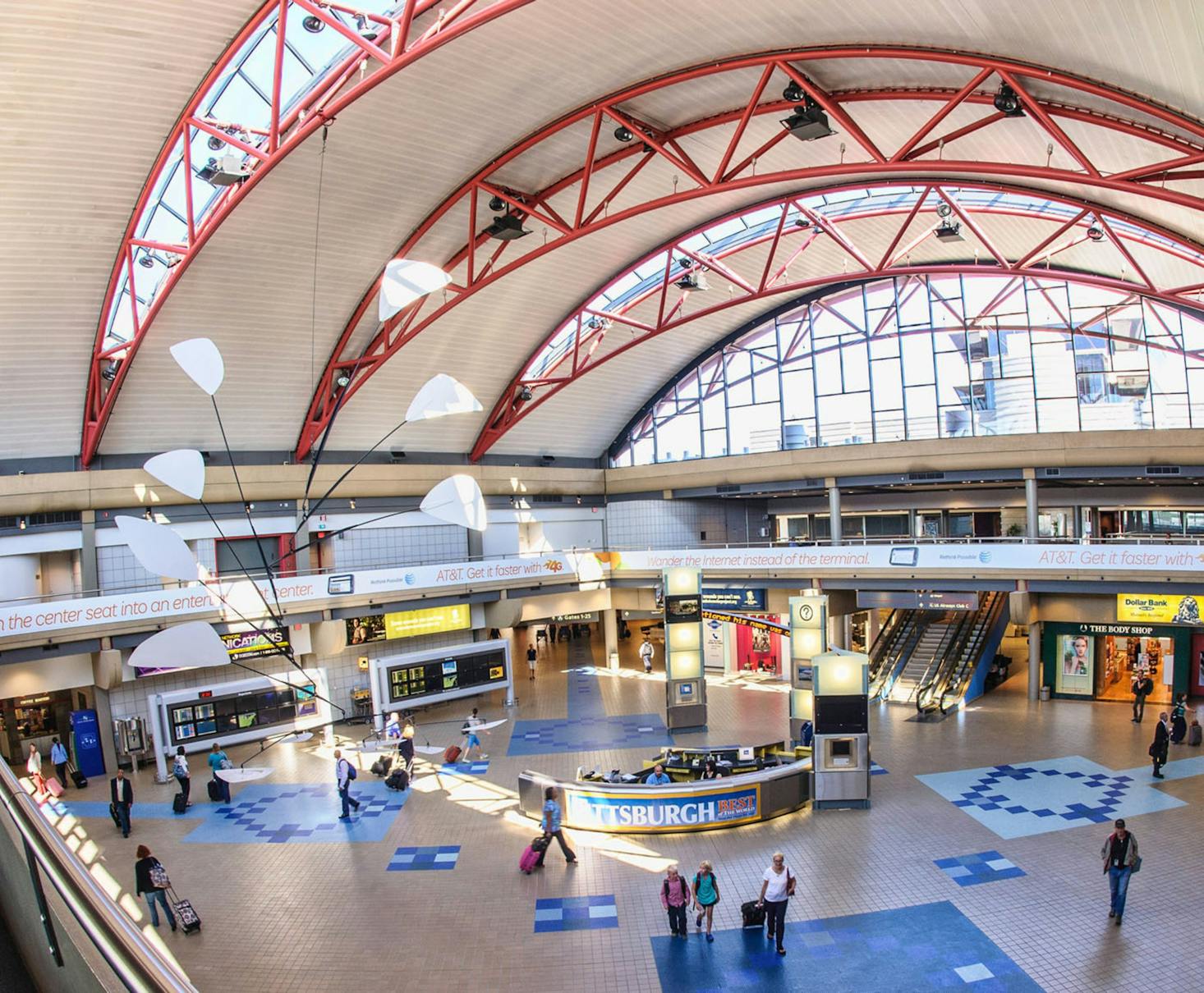 Brightly lit terminal of Pittsburgh Airport, featuring high arched ceilings with red beams and modern decor.