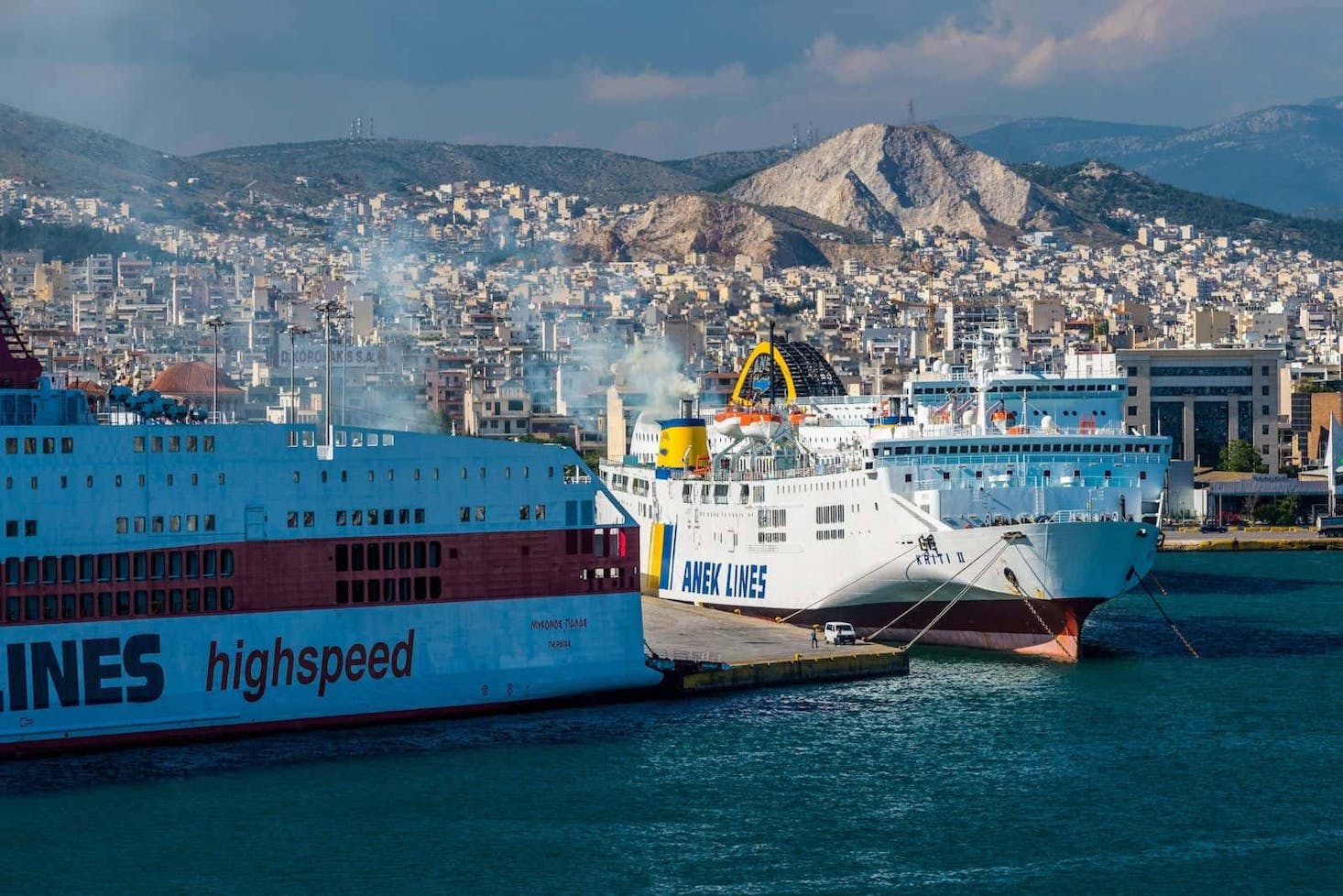 Ferries docked at Port of Piraeus with a cityscape and mountains in the background.