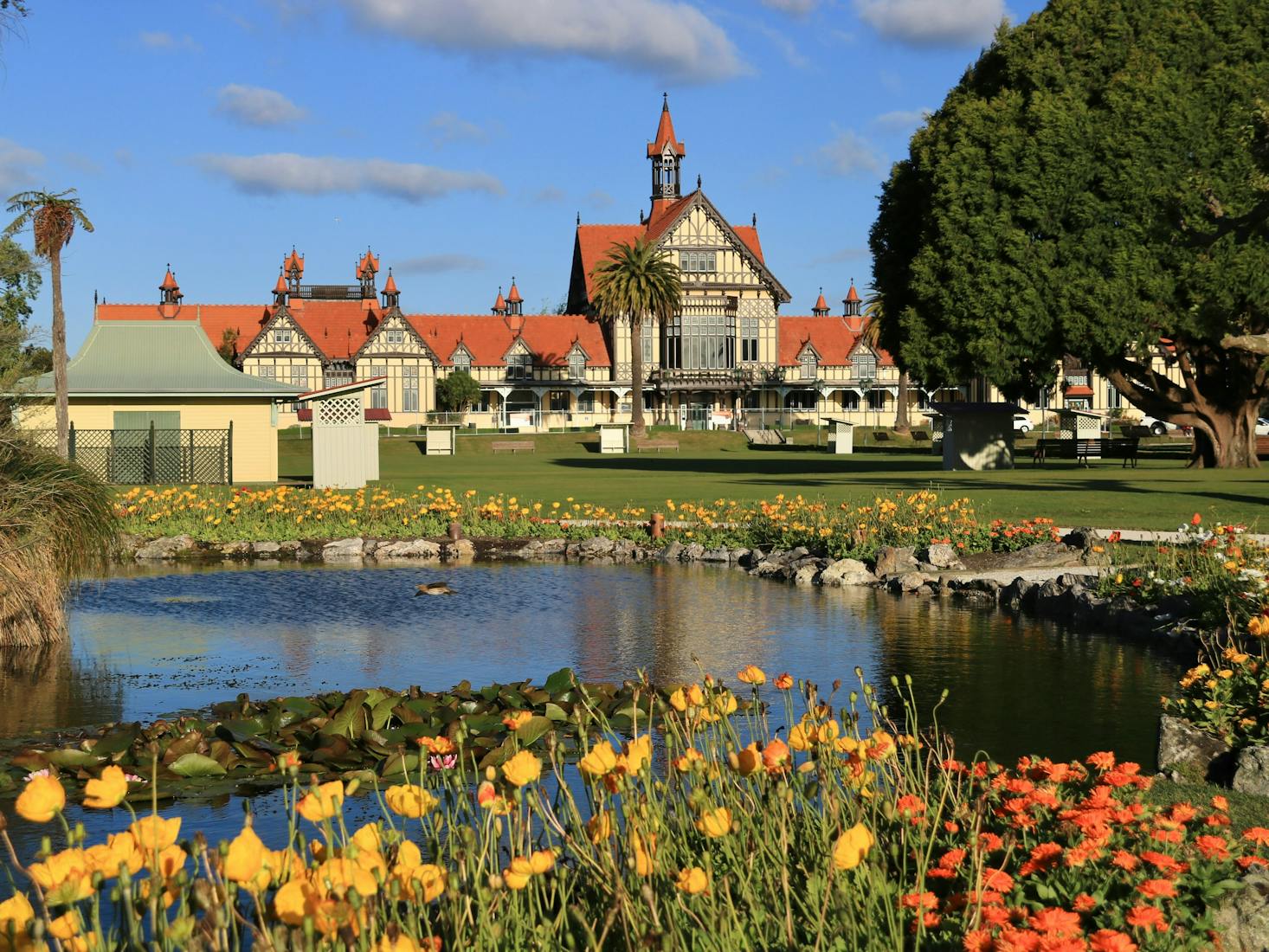 A picturesque building in Rotorua with red roofs and ornate architecture, surrounded by a lush garden