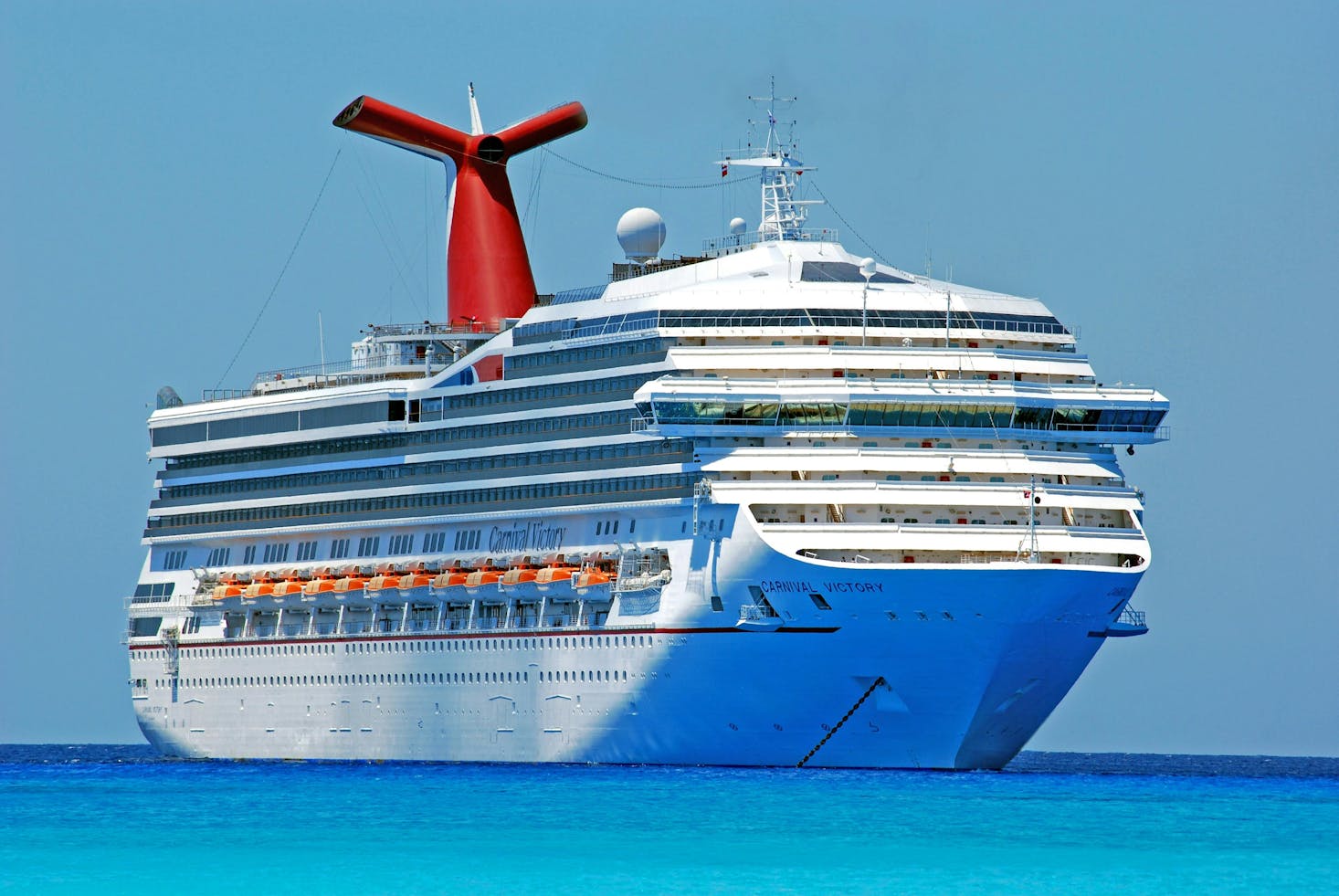 A large cruise ship docked in clear blue waters under a bright sky.