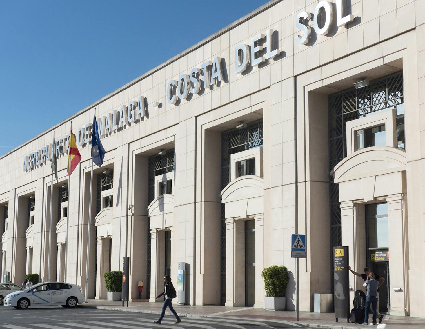 The exterior of Malaga-Costa del Sol Airport, featuring its grand entrance with flags and people walking near the building.