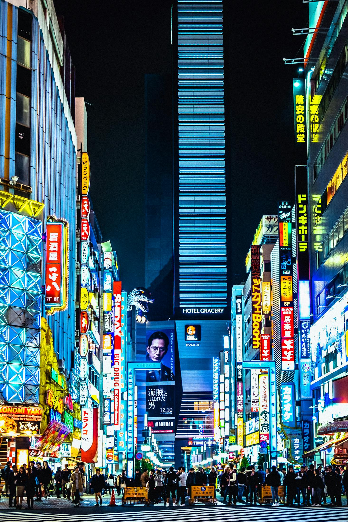 Vibrant street in Tokyo at night, illuminated by colorful signs and billboards, with crowds of people walking along the bustling avenue.