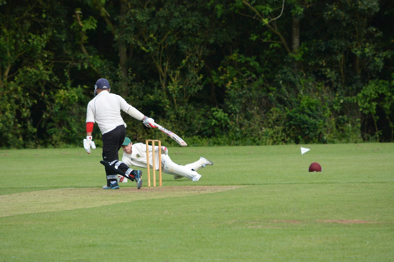 Two cricket players in action during an intensive match, with one player on the ground