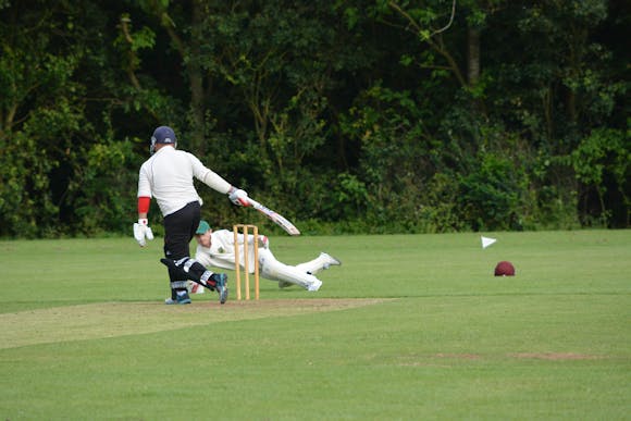 Two cricket players in action during an intensive match, with one player on the ground