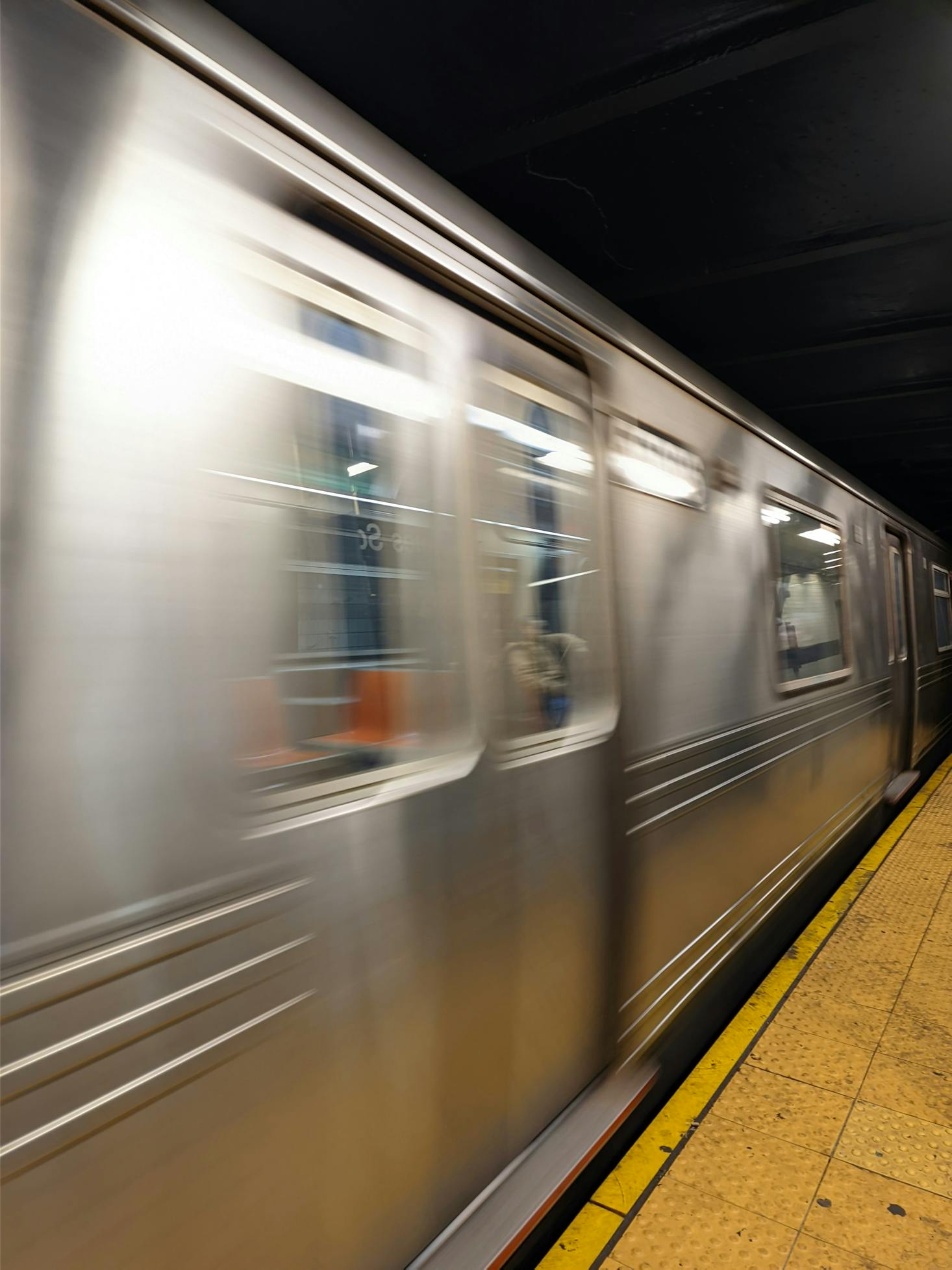 A silver subway train quickly pulls away from a yellow platform