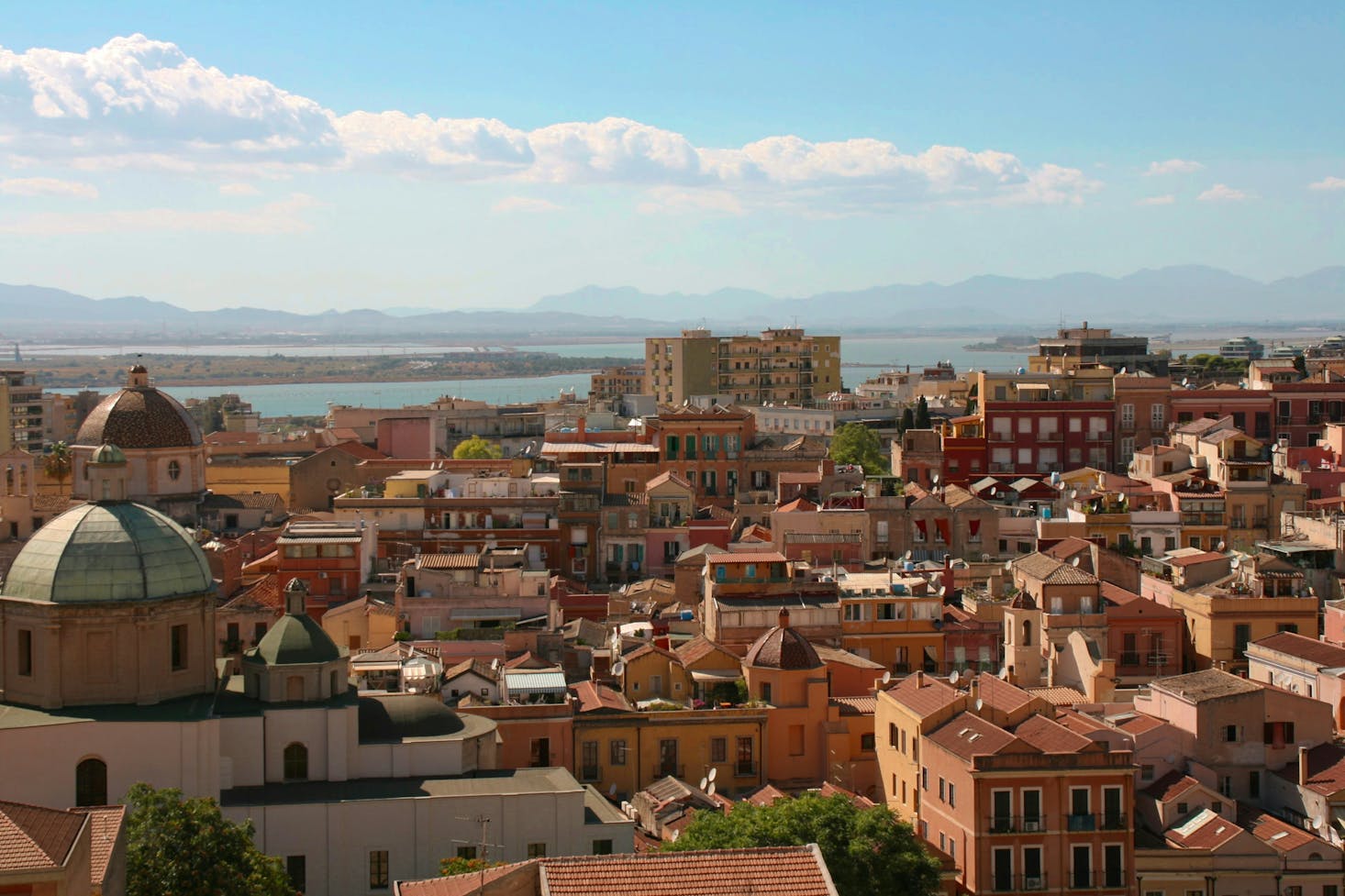 Vista dall'alto sui tetti di Cagliari, con mare sullo sfondo e cielo azzurro