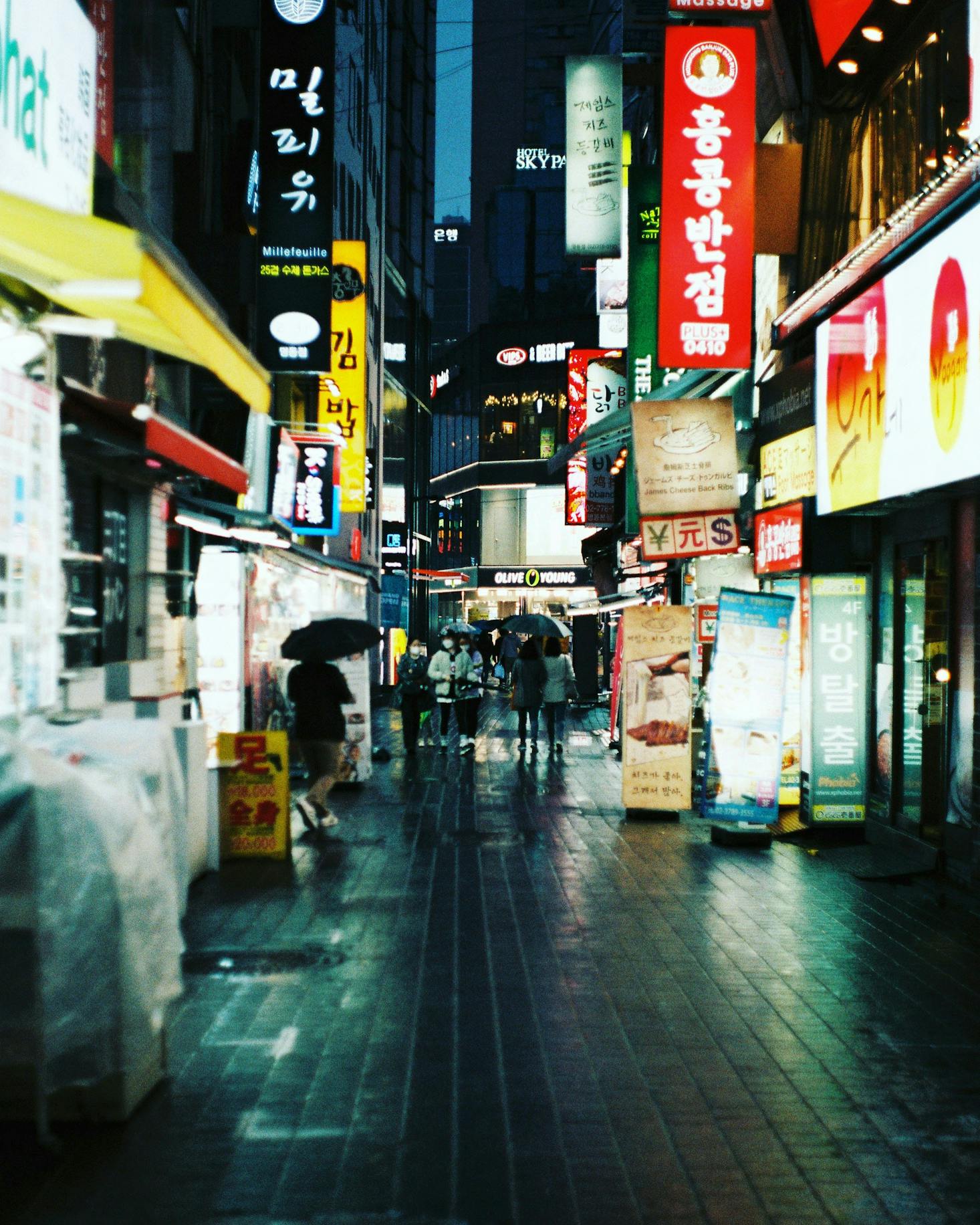 People walking in the rain in the Myeongdong neighborhood of Seoul lit up by neon store signs