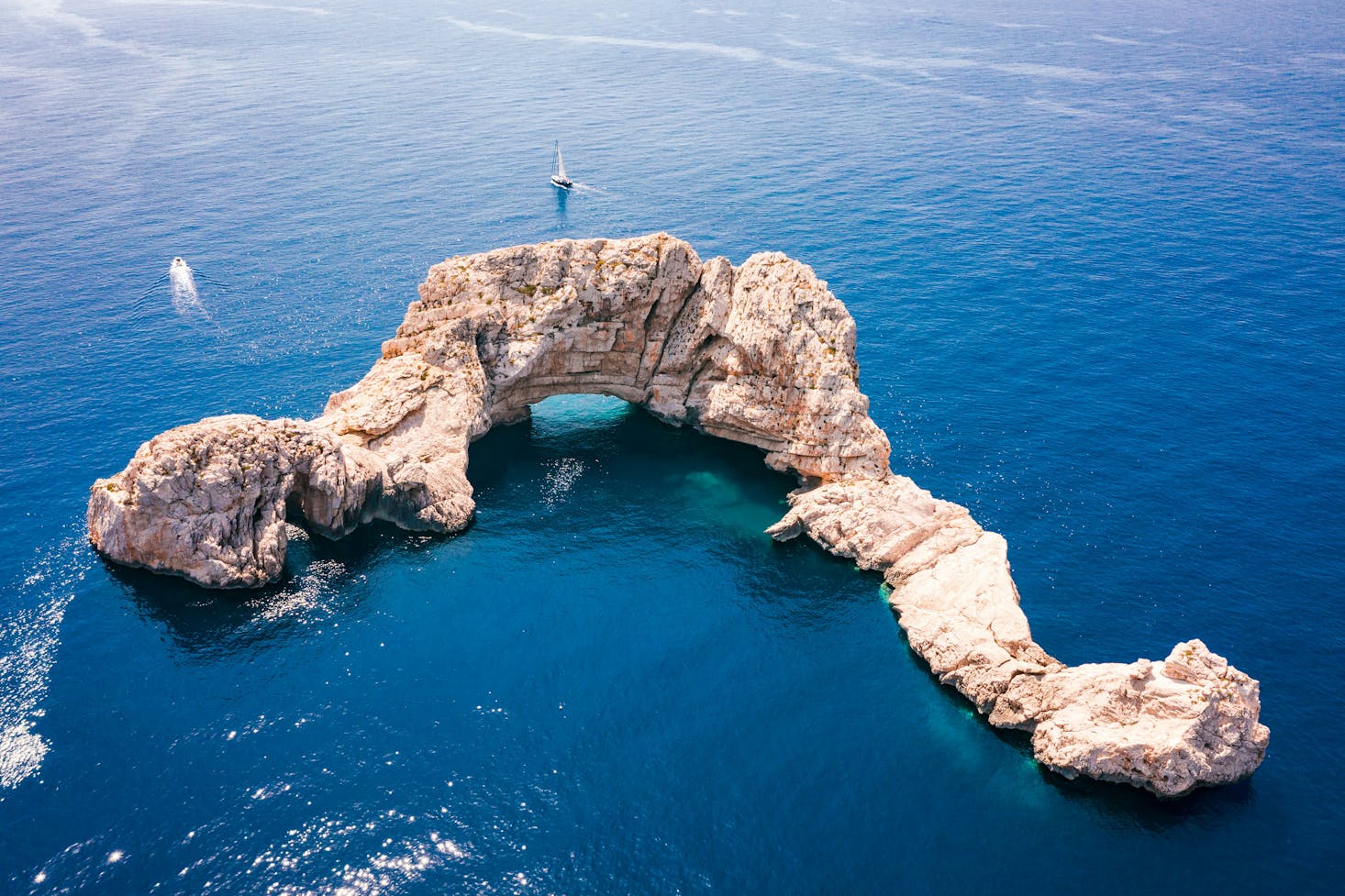 Mare blu di Ibiza, con scoglio iconico e barche sullo sfondo