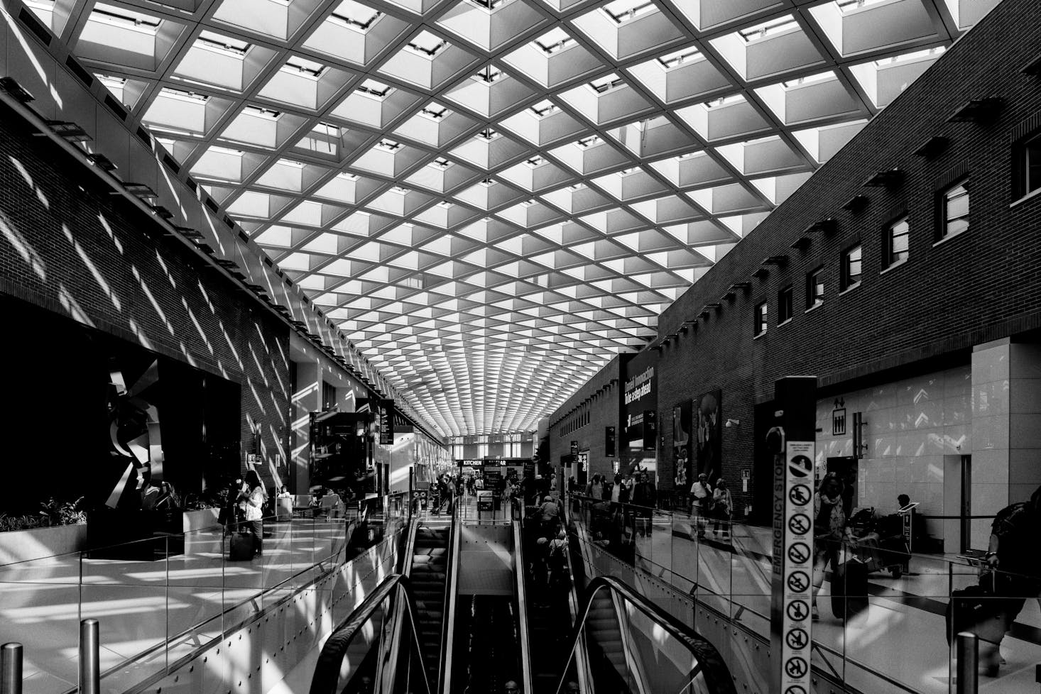 Interno dell'Aeroporto Marco Polo di Venezia, con caratteristico soffitto geometrico e viaggiatori che camminano 