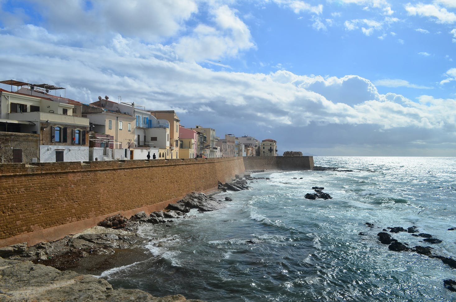 Vista sul lungomare di Alghero, con mare e scogli, cielo azzurro e case del centro