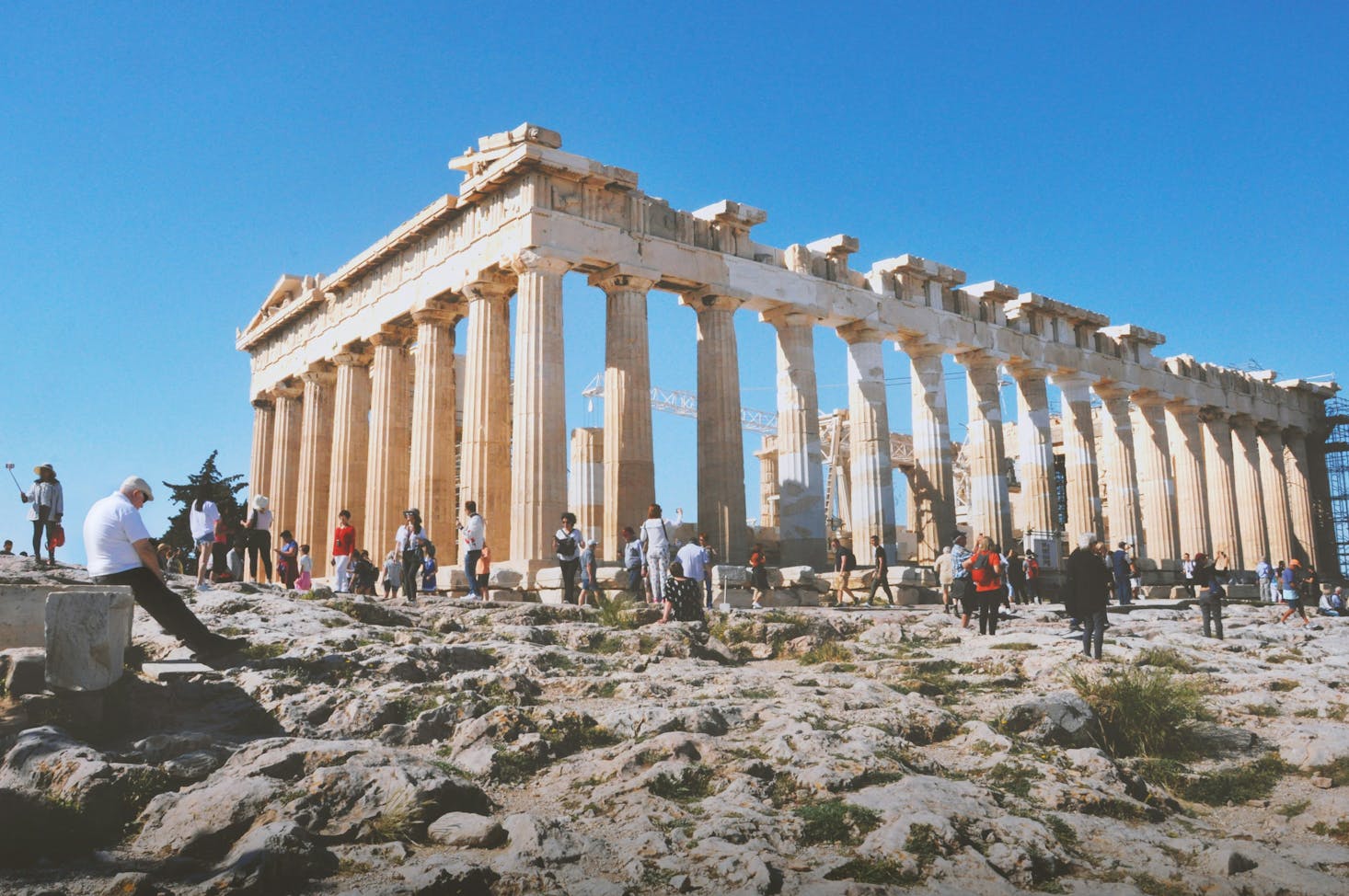 People standing around a ruined structure of white columns at the Acropolis in Athens