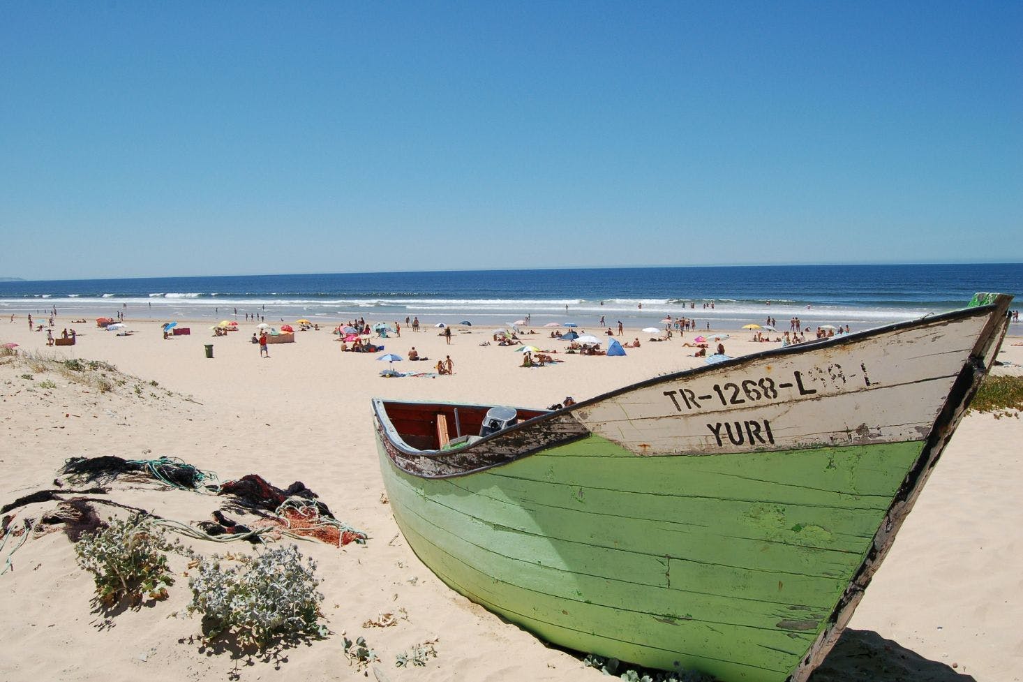 One of the sandy beaches near Lisbon with a vintage green Yuri boat and visitors enjoying in the background