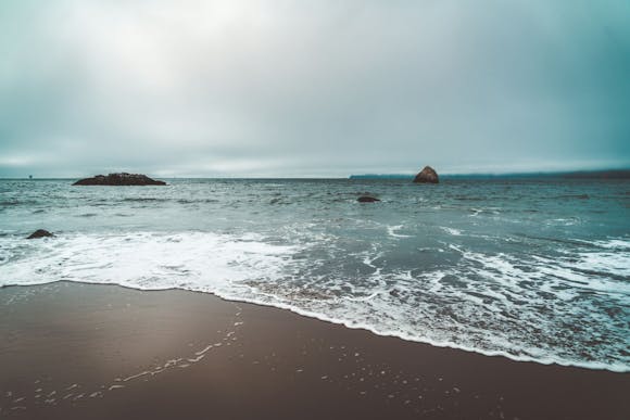 Dark brown sandy beach in San Francisco with foamy waves rolling in under a dark gray sky.