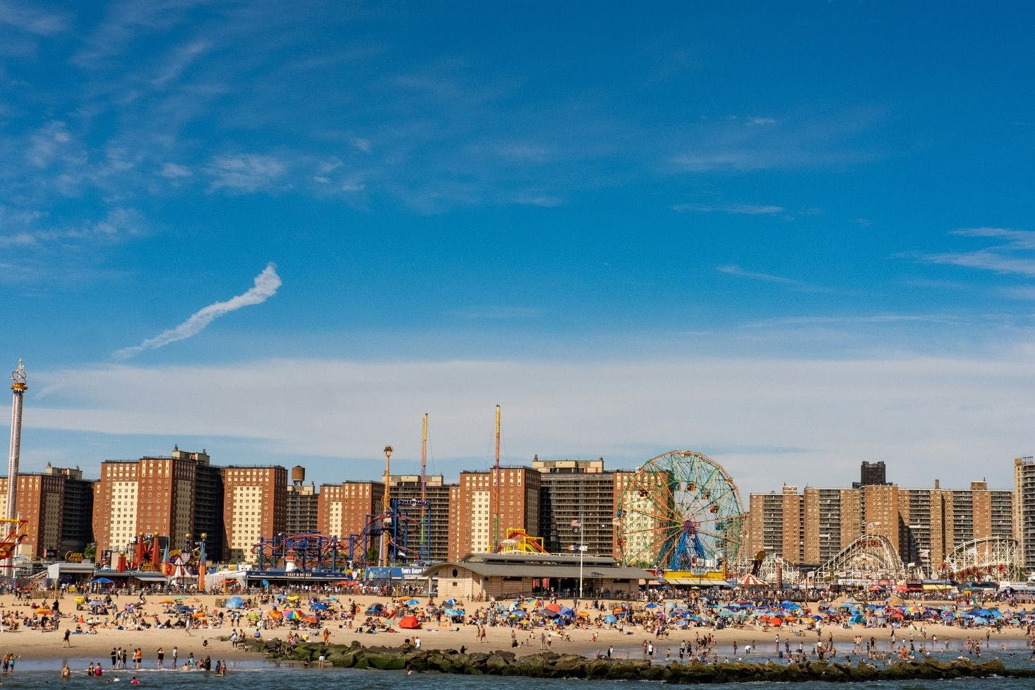 Busy sandy Coney Island beach with a Faris wheel and buildings in the background