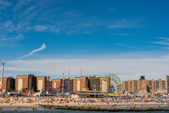 Busy sandy Coney Island beach with a Faris wheel and buildings in the background