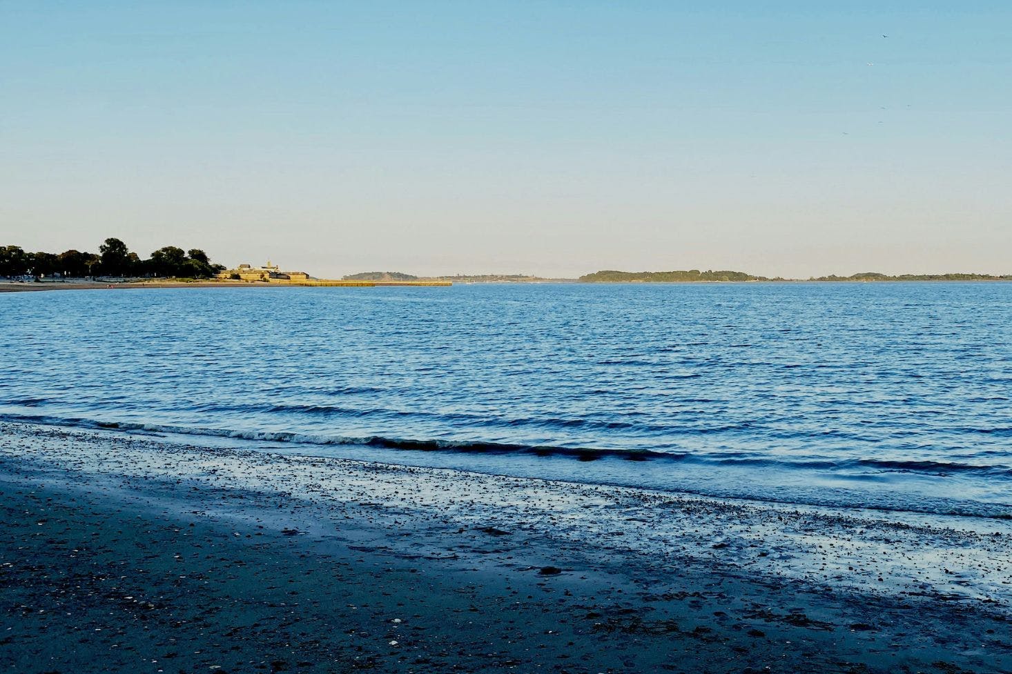 Sandy and pebbly Carson Beach in Boston featuring the dark blue water of Boston Harbor under a clear sky