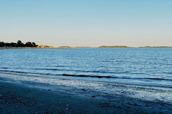 Sandy and pebbly Carson Beach in Boston featuring the dark blue water of Boston Harbor under a clear sky