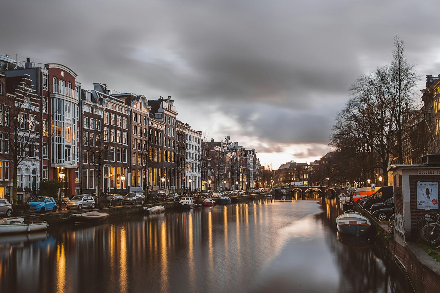 Vista su canale di Amsterdam, con edifici ai lati e luci della città specchiati nell'acqua, e con cielo scuro sullo sfondo