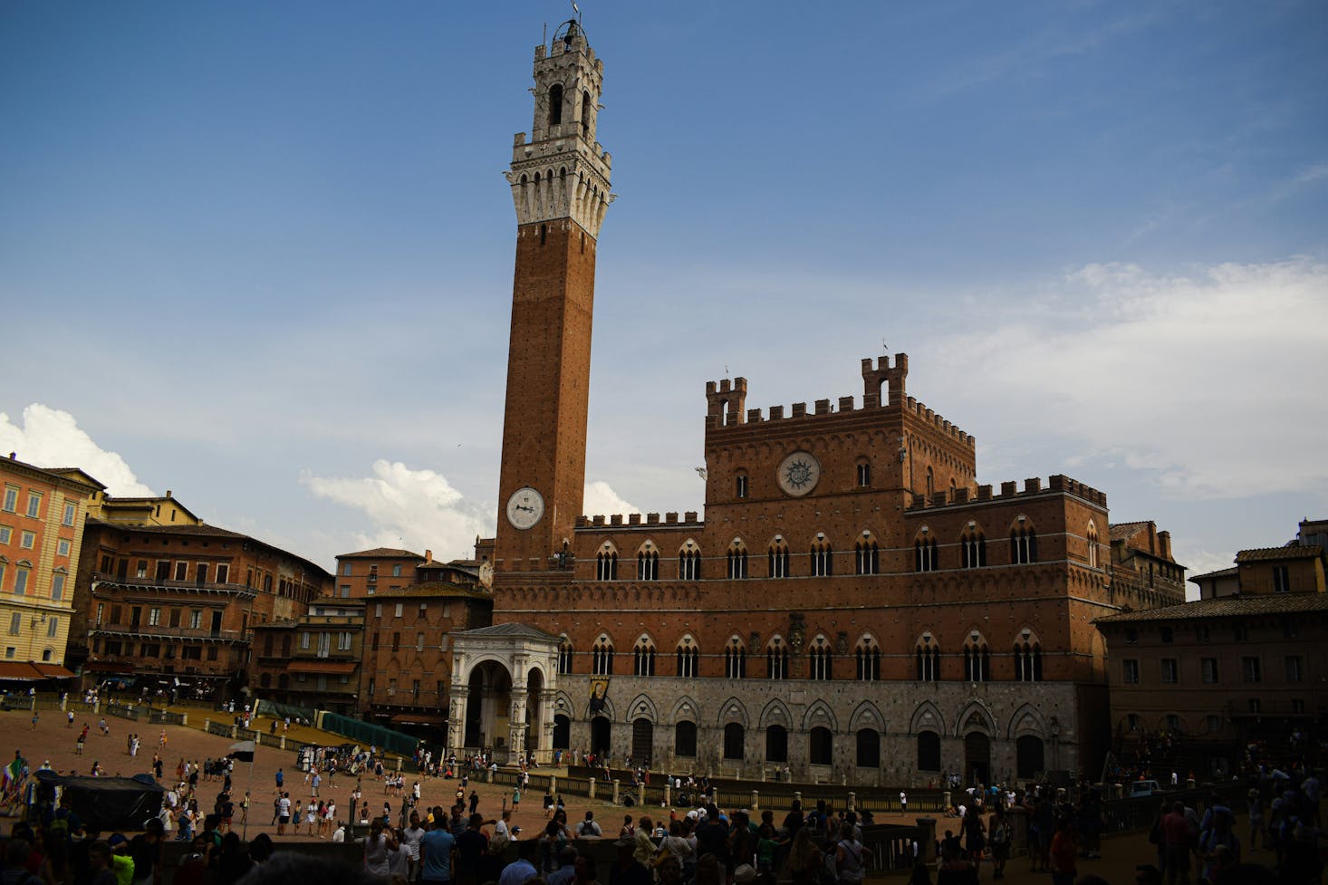 Persone che passeggiano in Piazza del Campo, a Siena, con attenzione al palazzo comunale e la Torre del Mangia