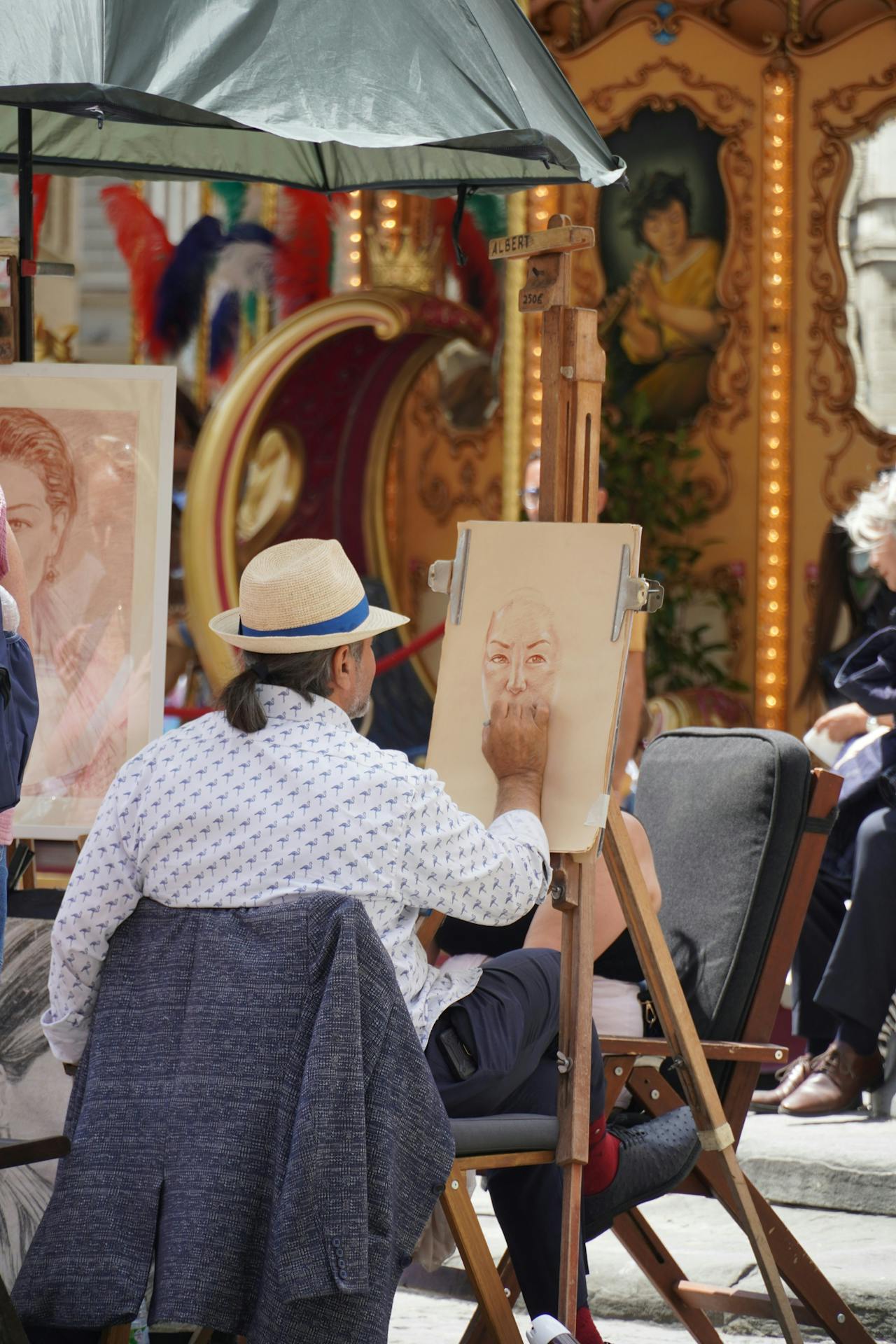 Street artist seated in a chair, creating a portrait outdoors while surrounded by people