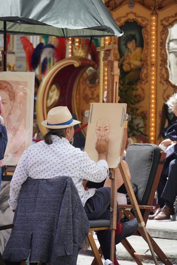 Street artist seated in a chair, creating a portrait outdoors while surrounded by people