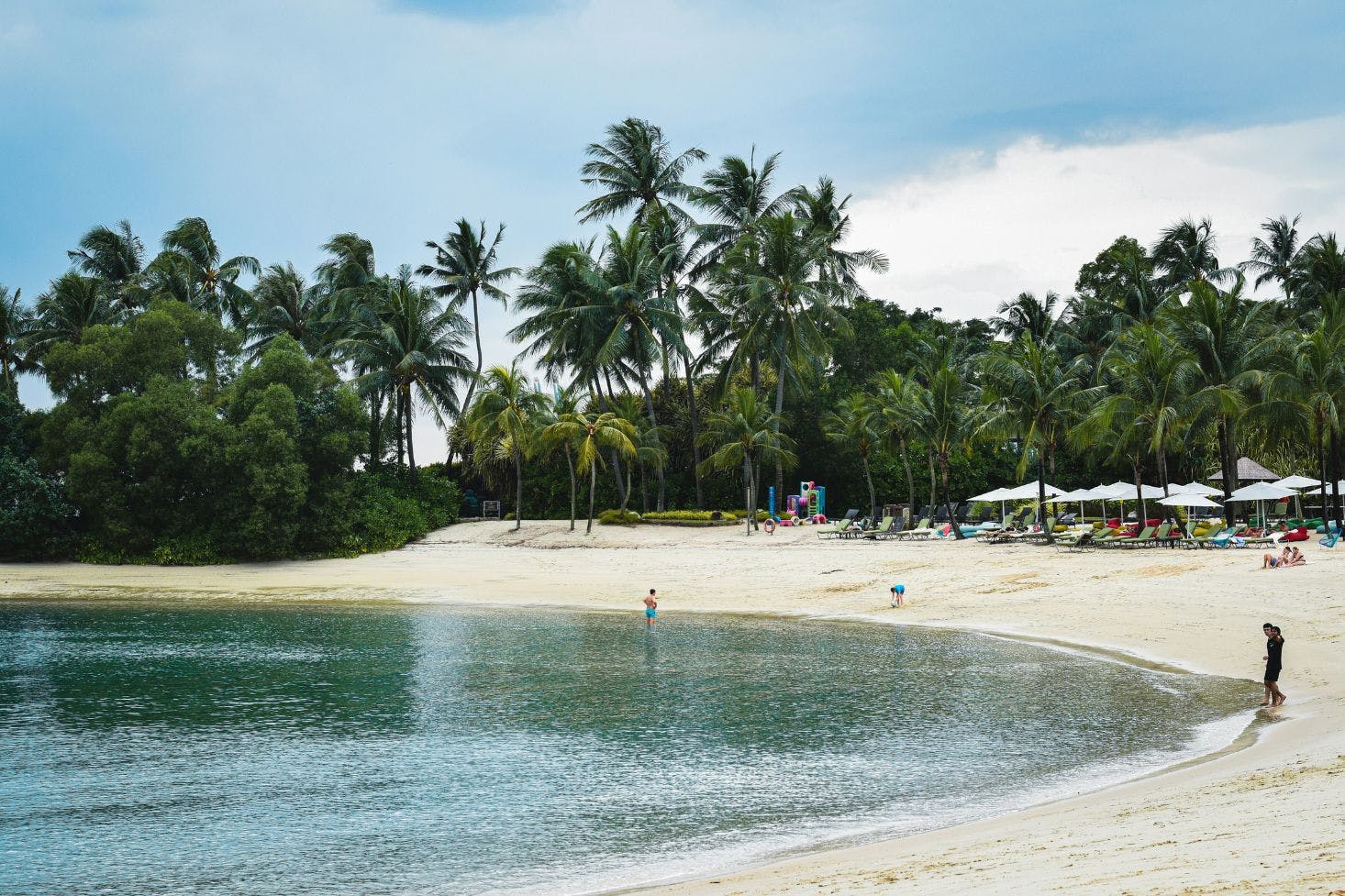 Sandy cove at Siloso Beach, Singapore with people, umbrellas, and beach beds