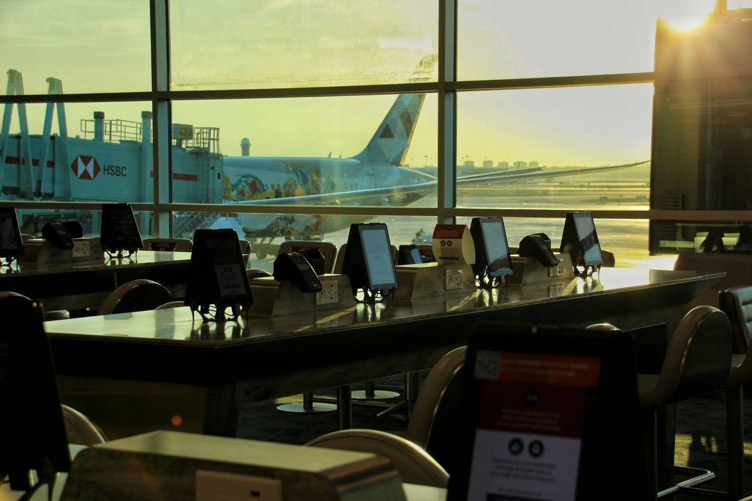 Seating area with tables, chairs, and screens by large windows at Pearson Airport, Toronto, with a plane visible outside