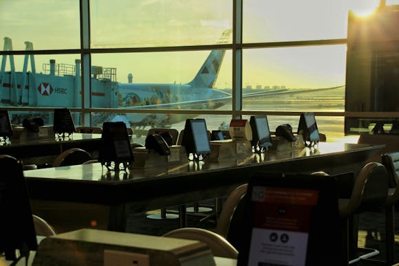 Seating area with tables, chairs, and screens by large windows at Pearson Airport, Toronto, with a plane visible outside