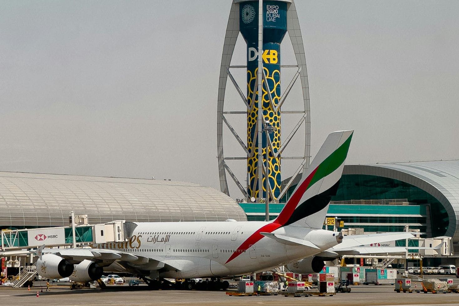 Dubai International Airport building with control tower, a parked plane, and surrounding airport vehicles