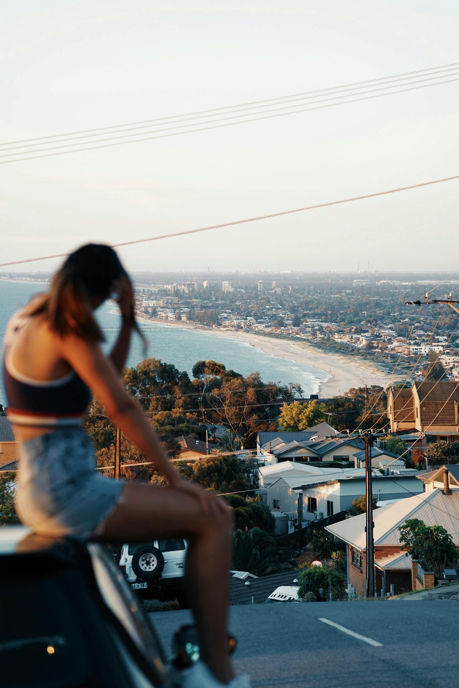 A woman sitting on a car looking out over Brighton Beach near Adelaide