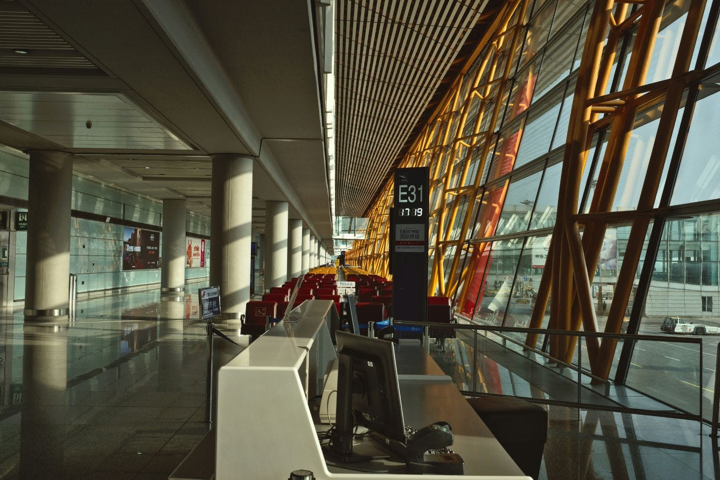 Beijing International Airport counter by large windows, with a seating area of burgundy chairs and a corridor in view