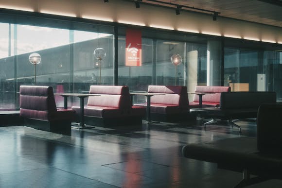 Seating area with red benches and tables near a window, with a Wi-Fi sign at Vienna Airport